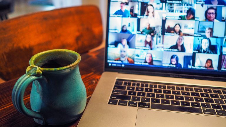 a green earthenware mug sits beside a life coach's open laptop with a videoconference full of clients