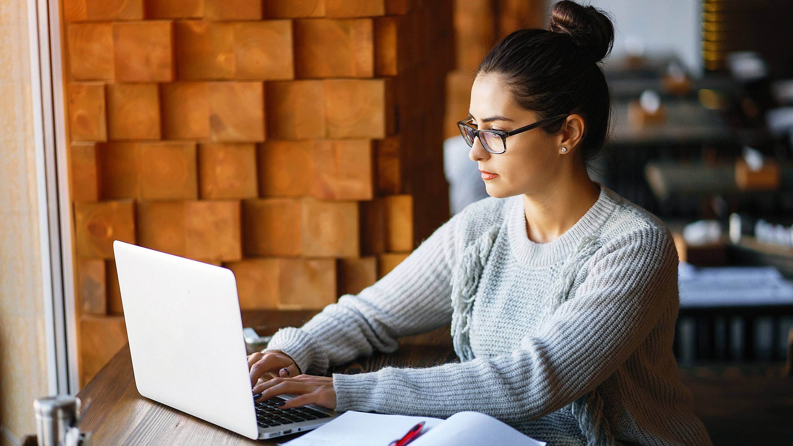 A woman in glasses types on a laptop, presumably creating an online course.